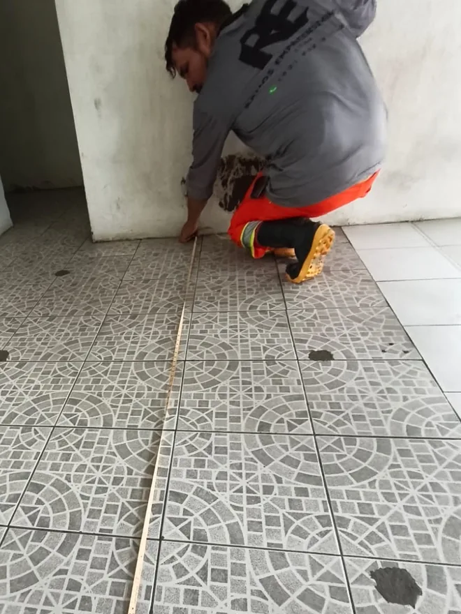 Operário da Ramos conferindo com trena o alinhamento do piso cerâmico assentado no interior da guarita reformada